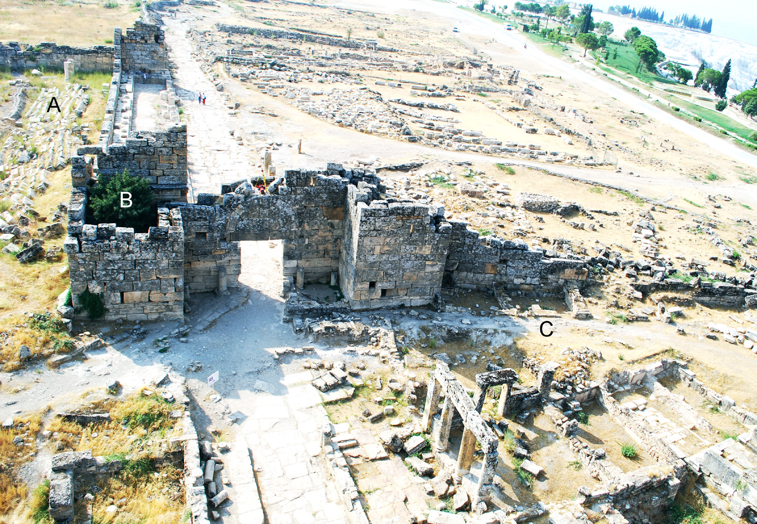 Fig. 4 – La Porta Nord in una ripresa aerea in cui sono ben visibili anche il crollo del muro di fondo del Ninfeo dei Tritoni (A), il lato breve dello stesso ninfeo, inglobato nella torre orientale della porta (B) e le strutture di epoca medio-bizantina che si addossano alla cortina esterna delle mura (C).