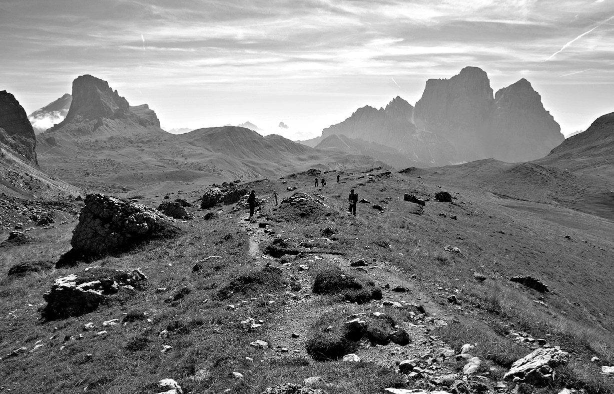 Fig. 3 – A typical Dolomitic landscape characterized by calcareous cliffs standing out on gentler slopes, with some archaeologists surveying natural erosions around a dirt path (photo D. Visentin).